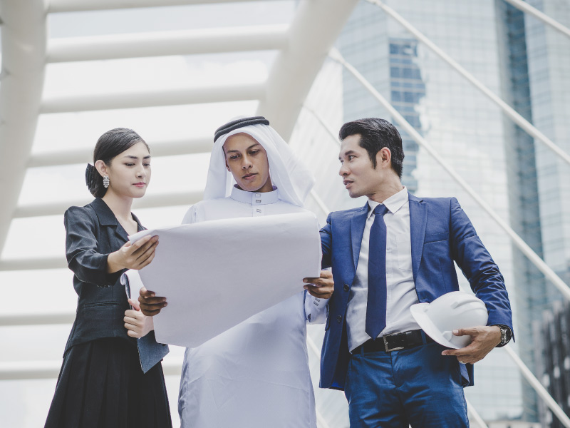 A group of Arabic business professionals engaged in a discussion about a business plan in an urban setting.